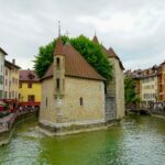 Vue pittoresque du Palais de l’Isle à Annecy, entouré de canaux et de bâtiments colorés aux façades anciennes.