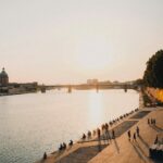 Coucher de soleil sur la Garonne à Toulouse, avec promeneurs sur les quais et le dôme de La Grave en arrière-plan.