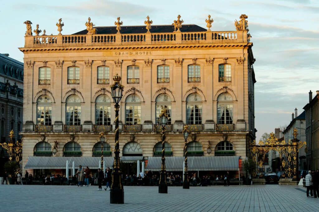 Façade élégante du Grand Hôtel de la Reine sur la place Stanislas à Nancy, baignée de lumière dorée.