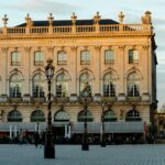 Façade élégante du Grand Hôtel de la Reine sur la place Stanislas à Nancy, baignée de lumière dorée.