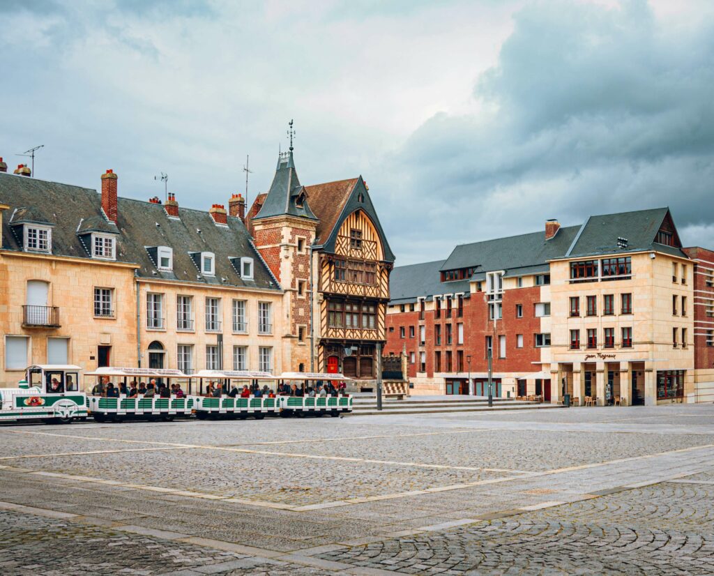 Place pavée d’Amiens avec maisons traditionnelles et petit train touristique, proche d’une agence immobilière Amiens.