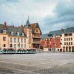 Place pavée d’Amiens avec maisons traditionnelles et petit train touristique, proche d’une agence immobilière Amiens.